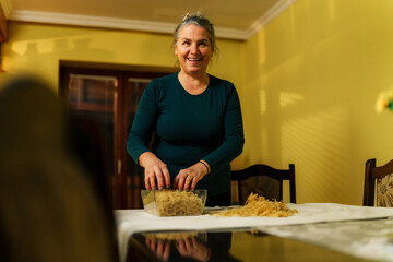 Happy senior woman arranging freshly harvested irish moss seaweed on her dining table, covered with a white tablecloth, for the drying process at home © DusanJelicic