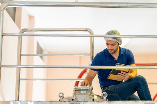 Winery manufacturing industry, wine tasting, brewery, alcohol liquor and wine making concept. Professional Caucasian man winemaker working in wine cellar with stainless steel barrels at wine factory.