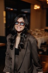 photo of a stylish brunette in glasses against the background of a restaurant interior with blurred...