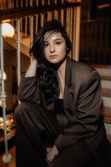 photo of a stylish brunette in an oversized pantsuit with a jacket against the background of a restaurant interior with blurred lights posing stylishly for a photo