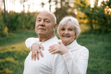 a nice couple of grandparents who look good and pose for a photo in light clothes in front of a park