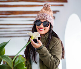 Retrato de mujer joven con gafas y gorra acariciando una flor blanca belleza, elegancia y cuidado...