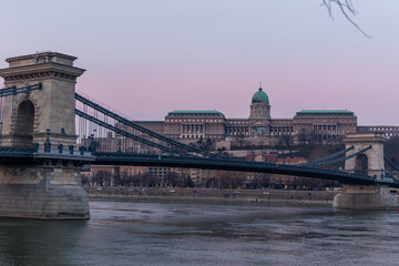 Fototapeta premium Széchenyi Chain Bridge crossing the Danube river with Buda Castle in the background during a purple sunset in Budapest