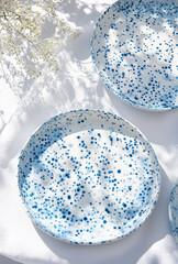 Obraz premium A collection of dishes – white porcelain bowls and cups with blue dots resting on a soft white tablecloth, with a vase of gypsophila flowers. Wedding table arrangement.