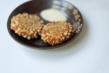 Crispy sabudana vada with yogurt dip on a black plate.







