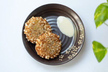 Crispy sabudana vada with yogurt dip on a black plate.







