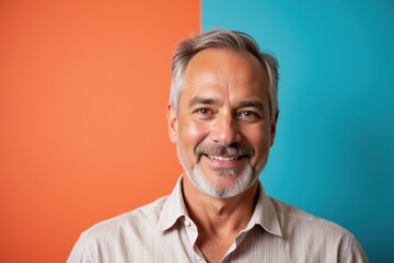 Fototapeta premium Middle-aged Caucasian Man with Gray Hair Smiling Against a Split Orange and Blue Background, Showcasing a Warm and Friendly Expression