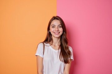 Obraz premium A Cheerful Young Woman with Long Brown Hair Smiling Against a Bright Orange and Pink Background, Radiating Joy and Positivity in a Studio Setting