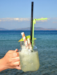 Girl holding melon fruit cocktail in jar glass on seashore
