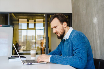 Concentrated man working on laptop in modern office