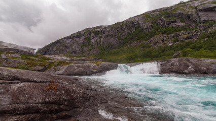 Majestic Norwegian Landscape Featuring a Cascading Waterfall Encircled by Dramatic Mountainous Terrain Under a Cloudy Sky