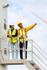Two engineers wearing safety equipment and standing on a wind turbine platform, performing...