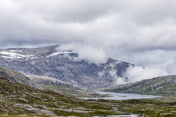 Majestic Norwegian Landscape: Serene Lakes and Dramatic Mountains Under a Cloudy Sky, Showcasing the Untamed Beauty of Nature's Elements in a Captivating Wilderness Setting