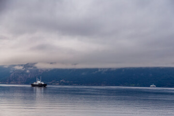 Obraz premium A Tranquil Scene of Boats on Calm Waters Under Overcast Skies in a Picturesque Mountainous Landscape with Soft Reflections and Serene Ambiance