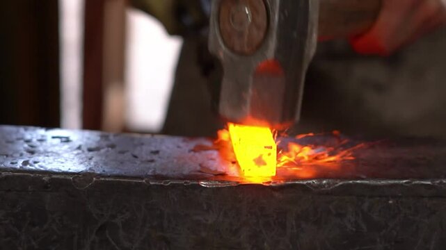 Blacksmith forging heated steel bar on anvil with hammer