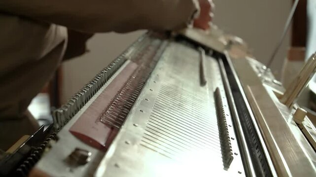 Close-up of artisan hands operating a manual knitting machine in a workshop setting.