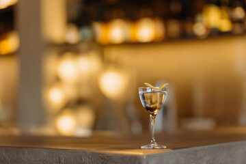 A sophisticated cocktail glass adorned with a lemon twist sits elegantly on the bar, surrounded by a warm, inviting ambiance.