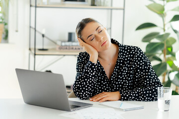 Tired overworked caucasian businesswoman, sitting at a desk with laptop with eyes closed, resting...