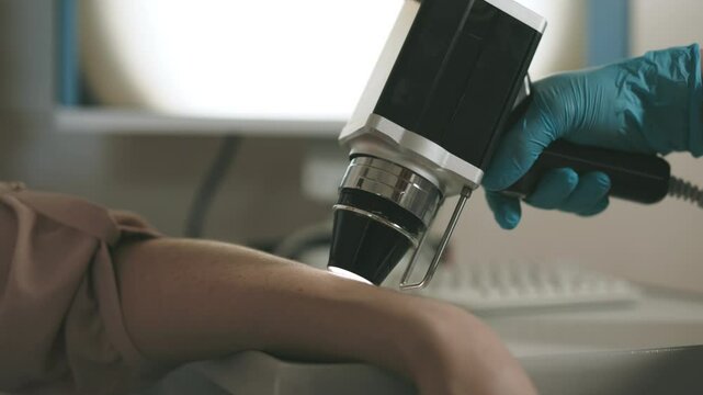 A dermatologist examines the skin of a young patient using advanced equipment, displaying cellular structure on the screen for analysis. Concept diagnosing skin diseases