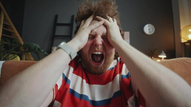 Young cheerful man yelling excitedly, pulling his hair, giving thumbs up and celebrating goal while watching sports match on TV at home. POV, whip zoom shot