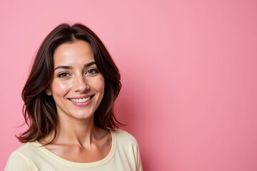 Fototapeta premium Smiling Young Woman with Dark Brown Hair Posing Against a Soft Pink Background, Radiating Confidence and Positivity