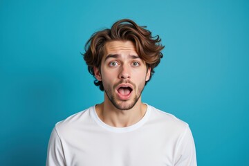 A Surprised Young Caucasian Male with Wavy Hair, Expressing Shock Against a Bright Blue Background
