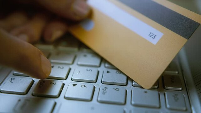 Entering CVV/CVC code on a laptop keyboard with a credit card in hand, online payment security, cyber fraud risk, digital transactions, e-commerce safety