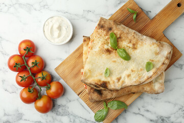 Halves of tasty calzone, basil, sauce and tomato on white marble table, flat lay