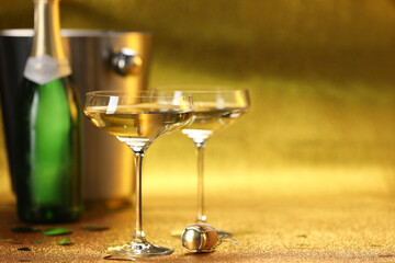 Champagne in glasses, bottle and ice bucket on golden background. Space for text