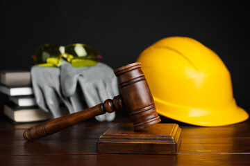 Accident at work concept. Gavel, books and construction worker's protective gear on wooden table,...