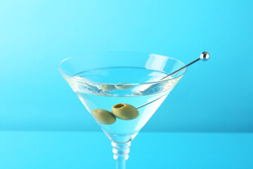 Martini cocktail with olives in glass on light blue background, closeup