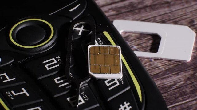 Closeup shot of a black and yellow cellphone and the parts of the sim card slot. Wood background. Communication. Showing the tool needed to open it. Camera slowly zooming out.