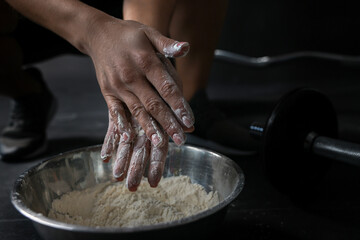 Woman applying talcum powder onto her hands above bowl before training in gym, closeup