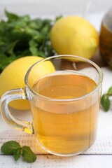 Aromatic mint tea with lemons and fresh leaves on white wooden table, closeup