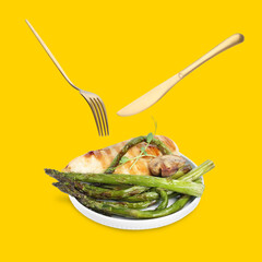 Cutlery in air over plate with tasty grilled chicken fillet and asparagus on golden background