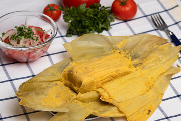 humitas en hojas de choclo, junto a una ensalada chilena de tomate y cebolla, atrás tomates rojos...