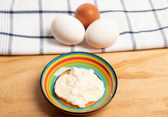 mayonesa servida en un colorido plato, al fondo un paño de cocina con 2 huevos blancos y 1 huevo de color café