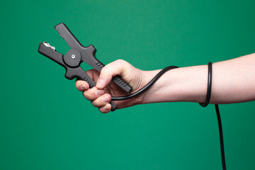 Automotive battery jumper cables in a man&rsquo;s hand, isolated on a green background. Studio shot with copy space, faceless framing.
