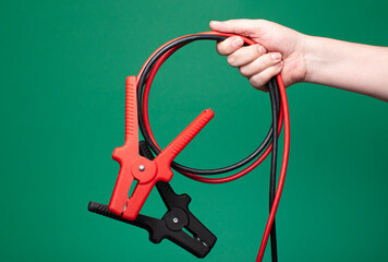 Hand of a man gripping jumper cables, isolated on a green background. Studio lighting, faceless composition, and room for text.
