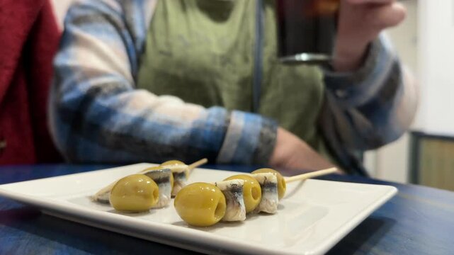 Closeup view, low angle shot, of a couple of two adult caucasian people chatting, casually toasting with vermouth, and enjoying spanish typical tapas inside.a bar. 4K