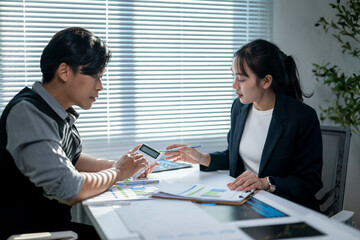 Two people are sitting at a desk, one of them is holding a calculator