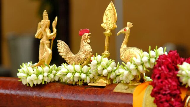 The image features an intricate golden sculpture of a rooster and a bird, adorned with jasmine flowers, symbolizing spirituality, tradition, and religious significance in cultural ceremonies.