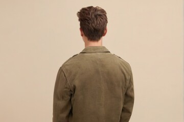 Young man in khaki jacket standing with back to camera, head turned, casual and relaxed vibe.