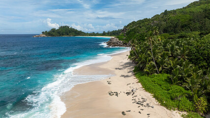 White sandy beach with turquoise waves and lush greenery in the background. Anse Boileau. Seychelles, Mahe.