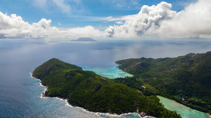 Aerial view of island surrounded by turquoise waters under a cloudy sky, with a distant horizon view. Seychelles, Mahe.