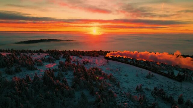 The famous narrow gauge railway of the Harz Mountains in Germany winding up the snow covered Brocken above the clouds during a bright red winter sunset. 