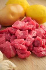 Freshly cut beef cubes with vegetables on a wooden surface