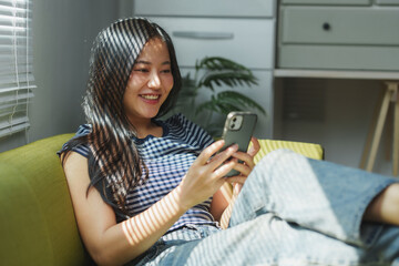 Young woman relaxing on sofa using smartphone at home