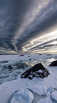 Wide shot of Frozen shoreline with snow covered boulders leading into a partially iced over ocean under a dramatic cloudy sky. Rugged beauty for winter seascapes. Vertical video backgrounds
