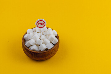 Sugar cubes in a wooden bowl with a stop sign on a bright yellow background